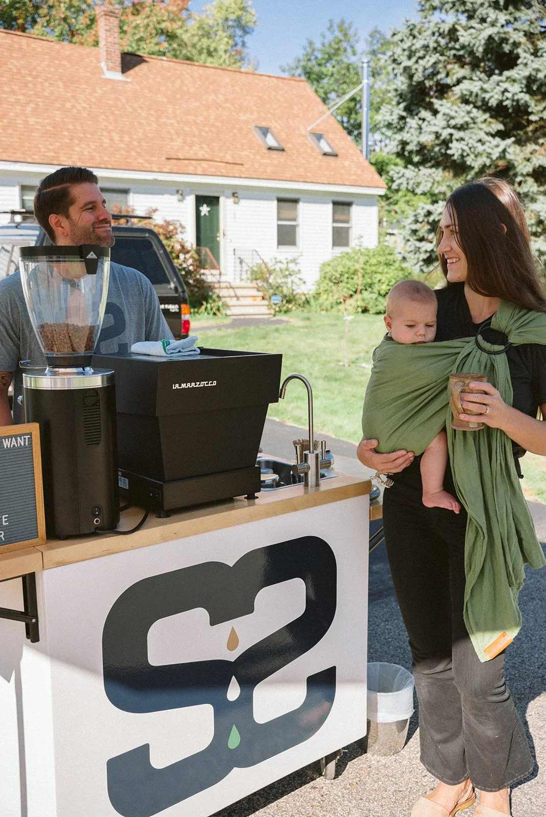 Kenny standing behind his mobile coffee cart with his wife and baby